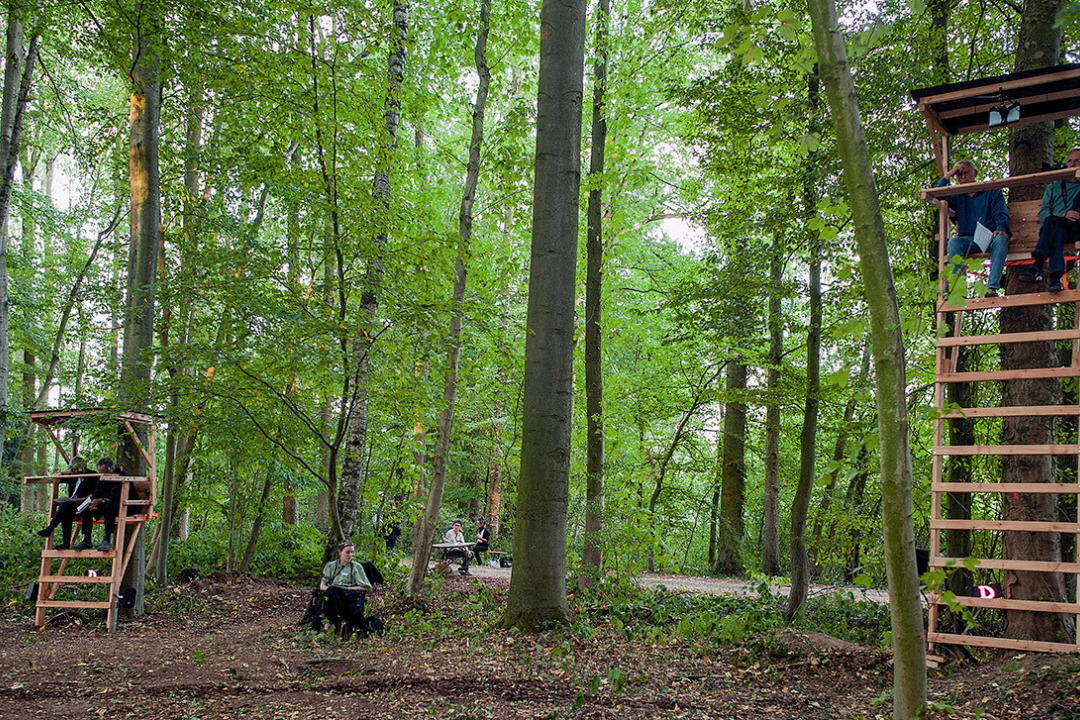 Waldst&uuml;ck abseits eines Wegs. An zwei B&auml;umen sind Hochsitze angebracht. Die Hochsitze bieten die M&ouml;glichkeit einer Sitzbank oben. Zudem sind sie verschieden hoch. Personen sitzen auf den Hochsitzen.