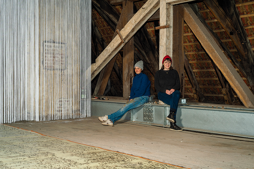 Ein Foto, das Emese Bodolay und Almut Pape zeigt. Die beiden sind Teil des Künstler*innenkollektivs »Anna Kpok«. Auf dem Foto sitzen sie auf dem Dachboden von Burg Hülshoff.
