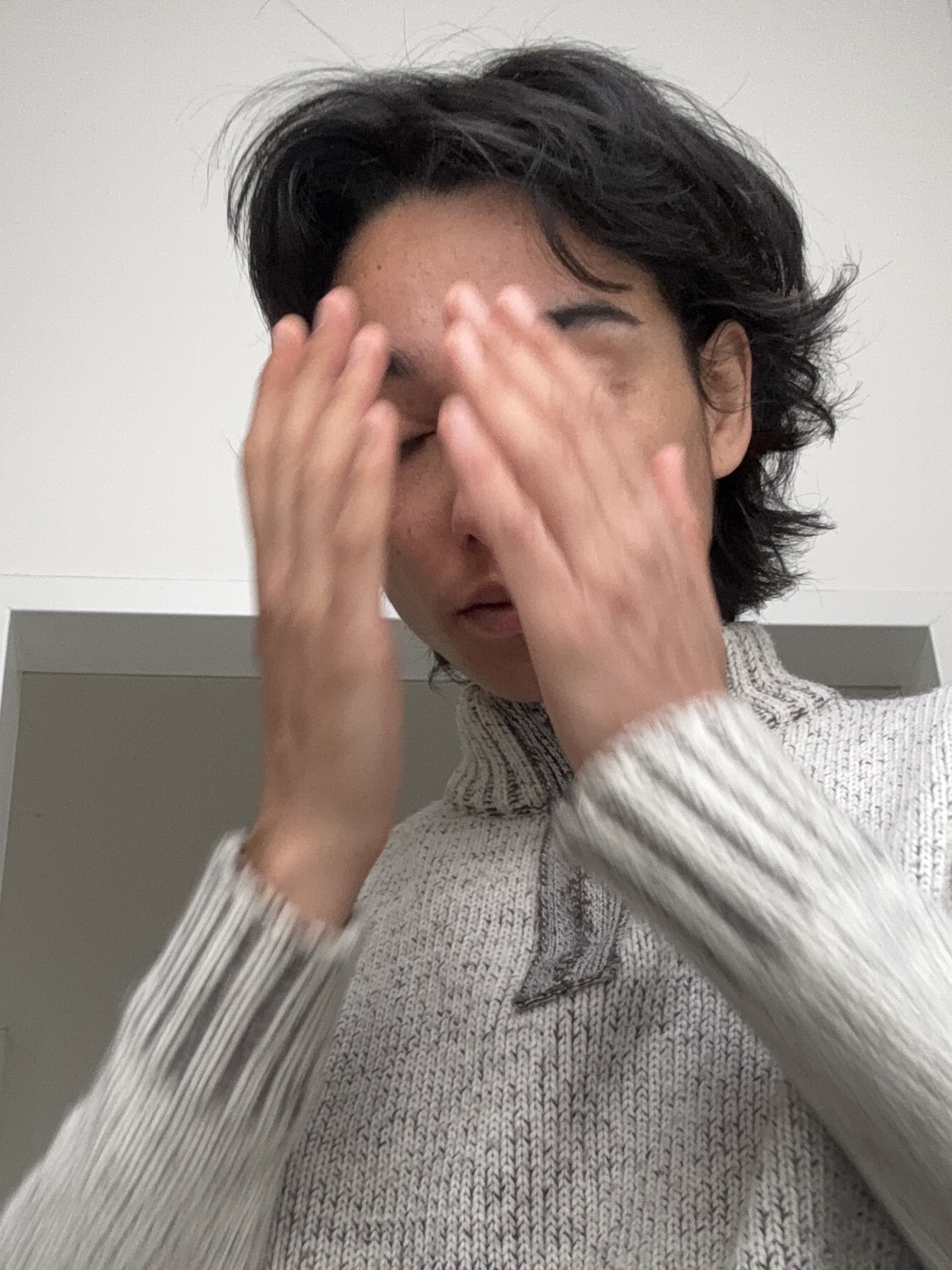 Portrait Foto von Miriam Stoney. Auf dem Foto hält sie sich die Hände vor das Gesicht. Weißer Hintergrung, grauer Pullover.