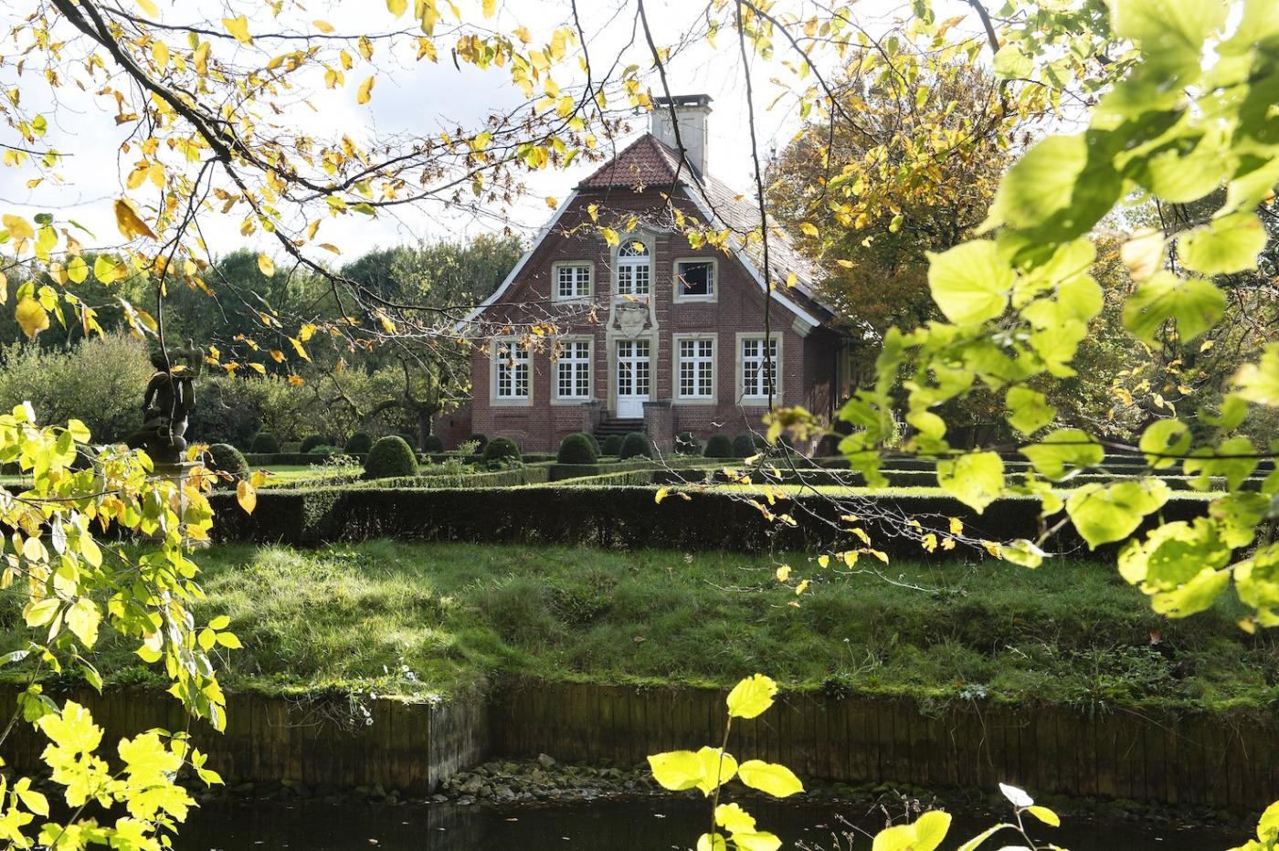 Das Bild zeigt Haus Rüschhaus von der Rückseite durch Blätter hindurch. Die Sonne strahlt auf das Haus.