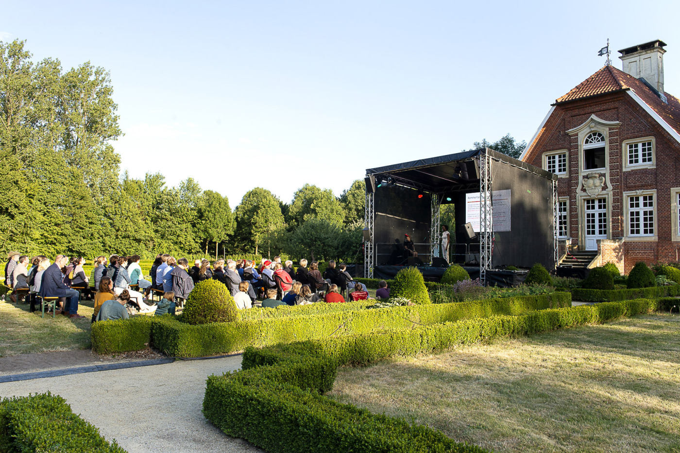 Publikum sitzt im Garten des Rüschhaus vor einer mobilen Bühne.