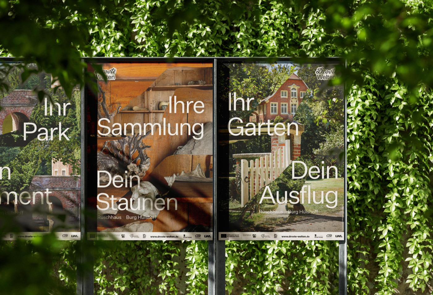 Fotografie einer Plakatwand, die von dichtem gr&uuml;nem Laub umgeben ist. Drei nebeneinander montierte Plakate zeigen Motive aus dem R&uuml;schhaus und der Burg H&uuml;lshoff und tragen die Texte &bdquo;Ihr Park&ldquo;, &bdquo;Ihre Sammlung&ldquo;, &bdquo;Ihre Garten&ldquo; und &bdquo;Dein Staunen&ldquo; sowie &bdquo;Dein Ausflug&ldquo;.