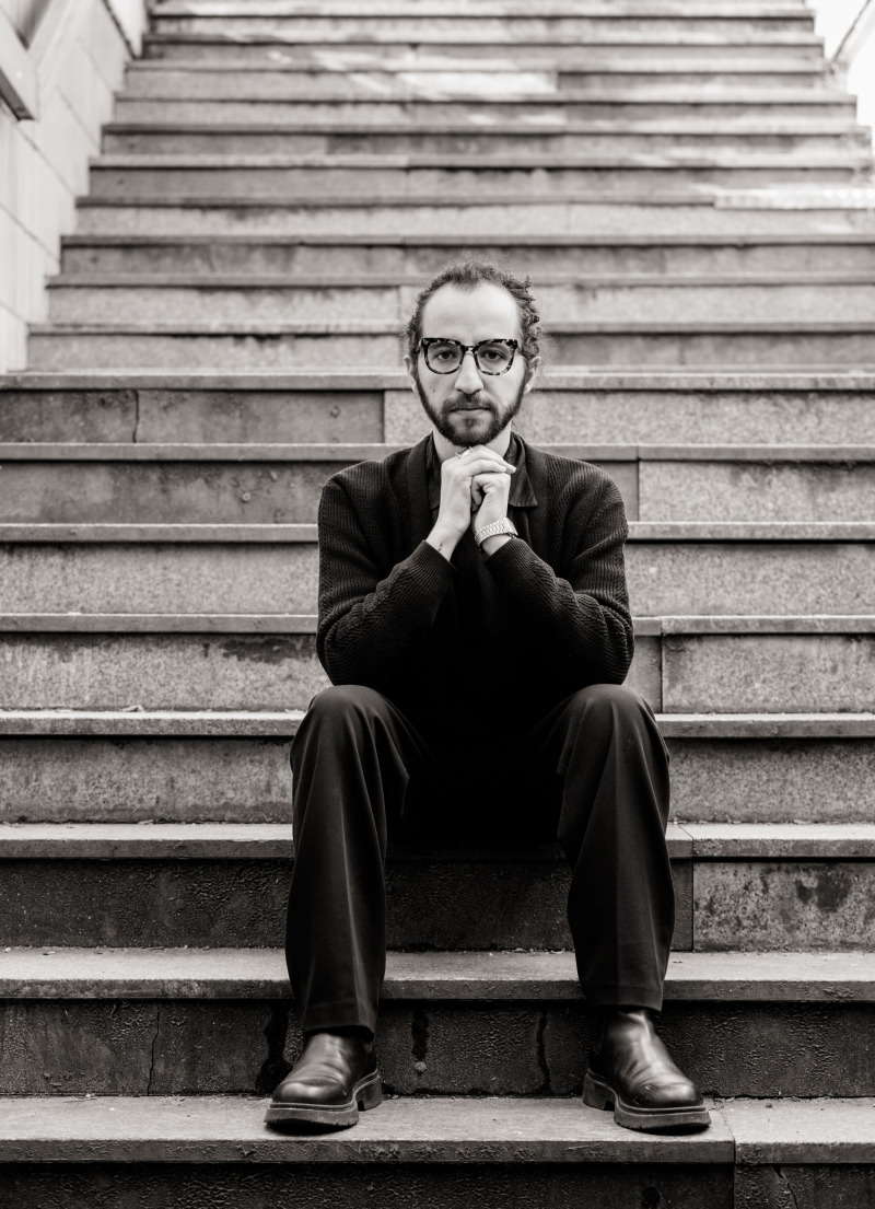 Portrait von Abdalrahman Alqalaq, sitzend auf einer Treppe. Das Foto ist schwarz-wei&szlig;. Copyright: Jan Hillnh&uuml;tter