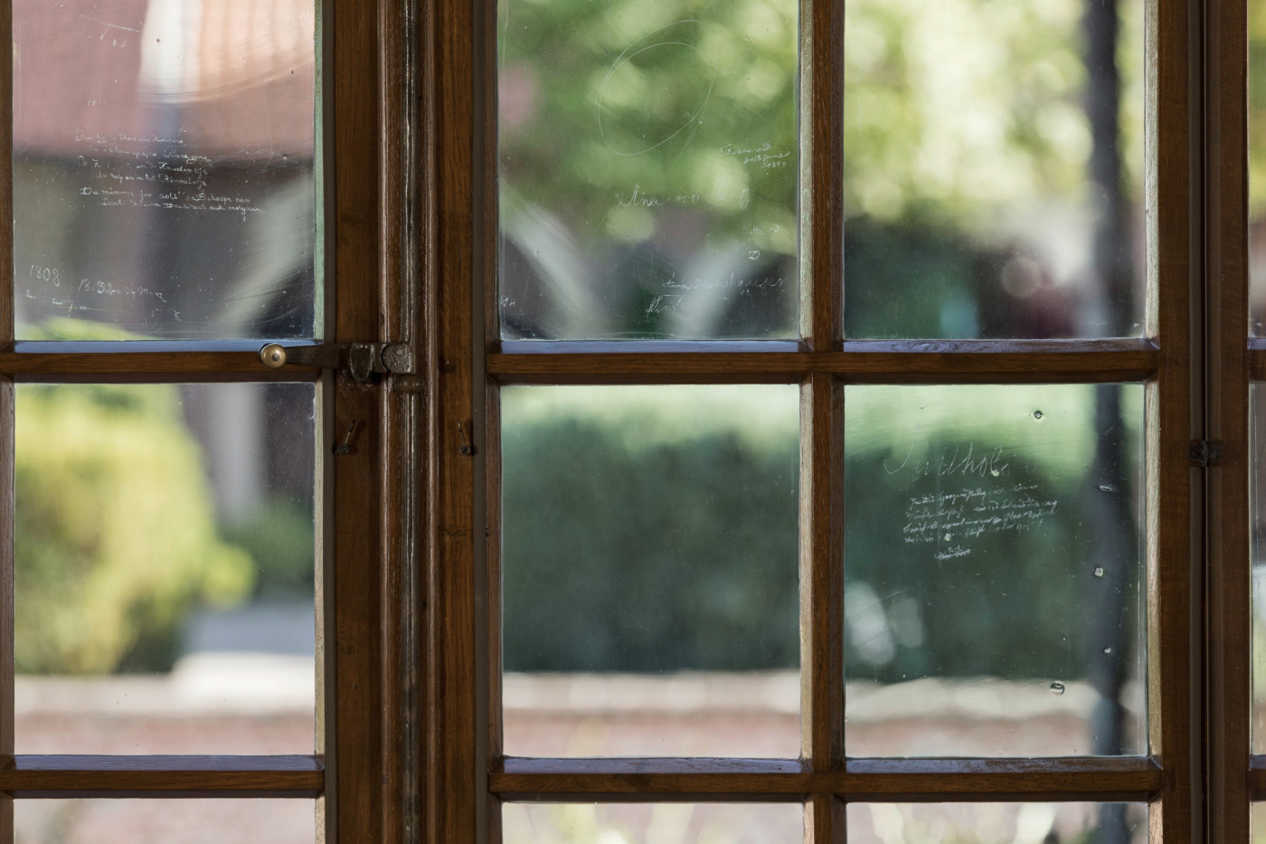Sprossenfenster mit dem eingeritzten Graffitto. Im Hintergrund, also au&szlig;erhalb liegt die Vorburg mit B&auml;umen und B&uuml;schen.